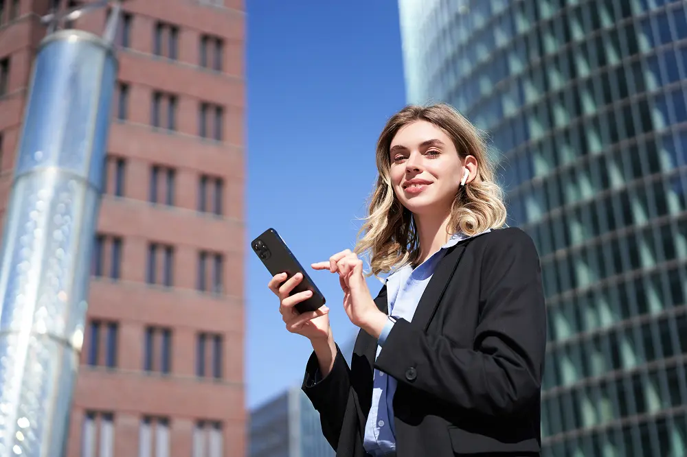 low-angle-shot-businesswoman-standing-street-sunny-day-holding-smartphone-using-app-tex 1.webp