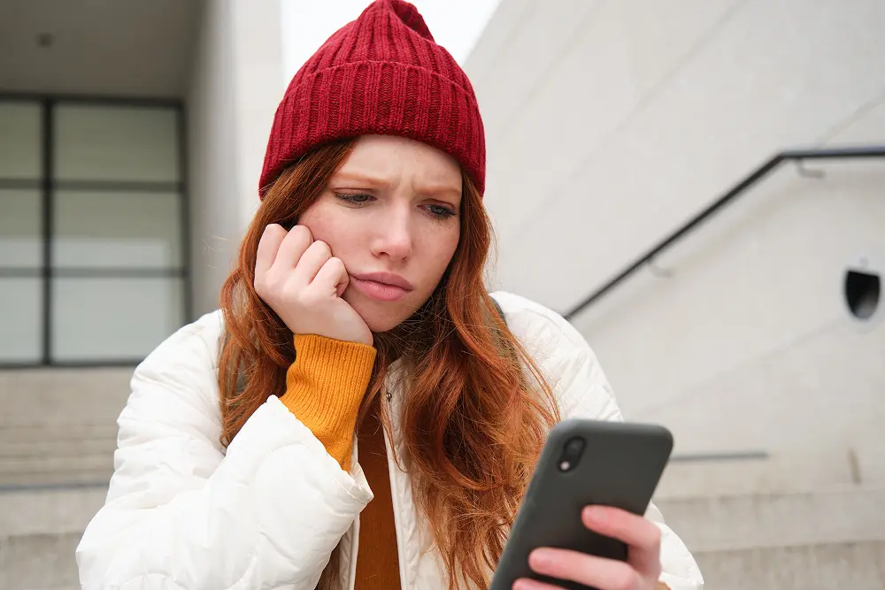 portrait-sad-redhead-girl-looks-upset-disappointed-smartphone-screen-reads-bad-news-text-m 1.webp